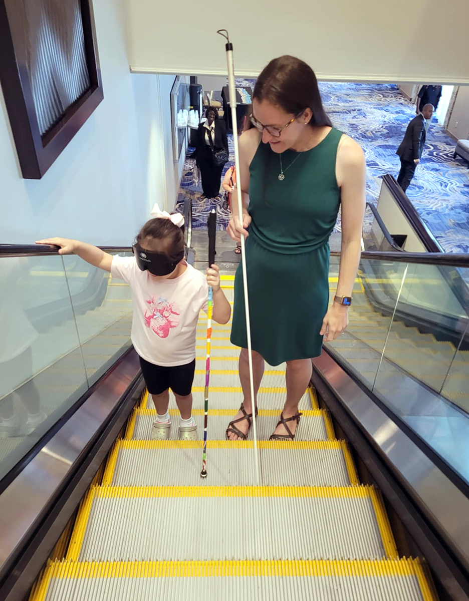 PursuingInnovation-Pic4 Katy Frets assisting and teaching a young child client, both of them are going up an escalator using mobility canes